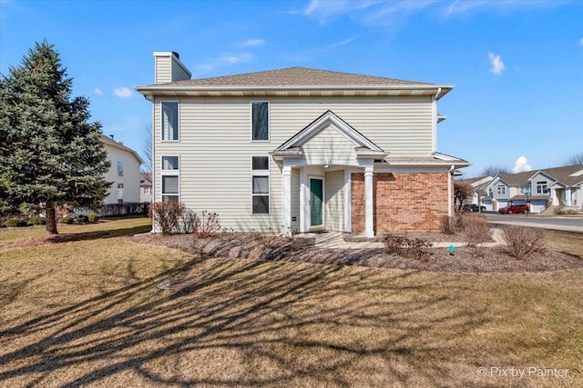 back of house with brick siding, a chimney, and a yard