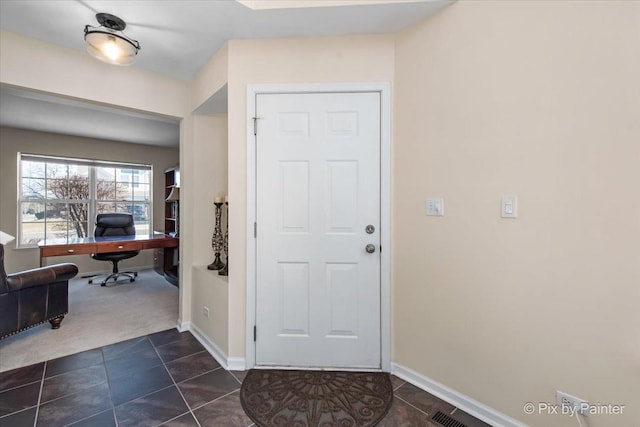 foyer with dark tile patterned floors, visible vents, baseboards, and dark colored carpet