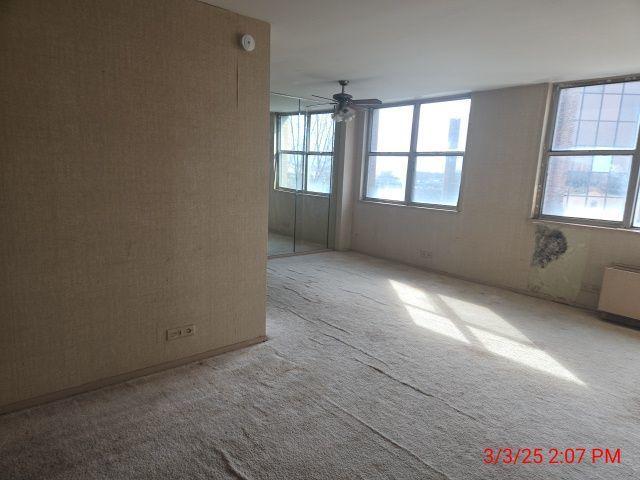 empty room featuring ceiling fan, carpet flooring, a wealth of natural light, and radiator