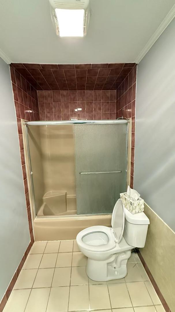 bathroom with bath / shower combo with glass door, crown molding, toilet, and tile patterned floors