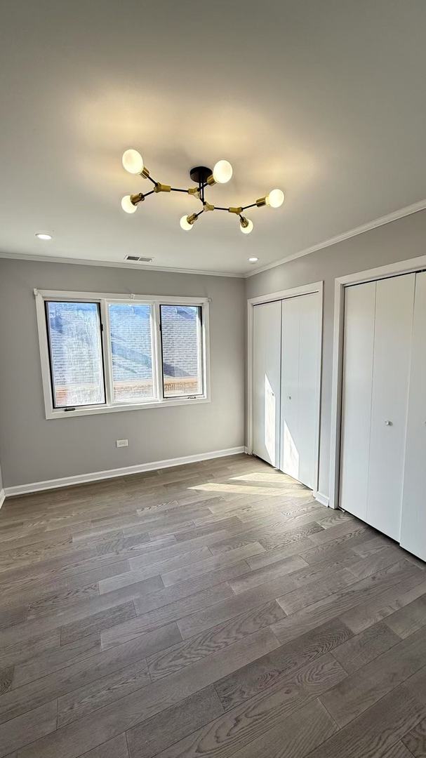 unfurnished bedroom with wood finished floors, visible vents, baseboards, two closets, and crown molding