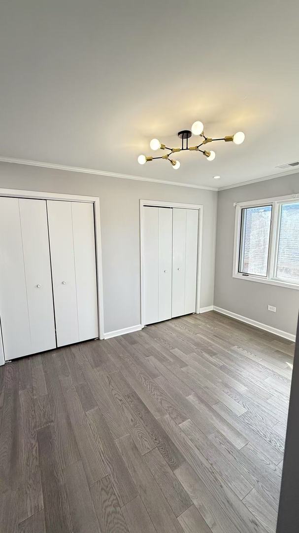 unfurnished bedroom featuring wood finished floors, visible vents, baseboards, and two closets