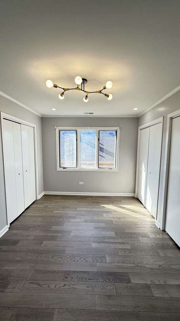 unfurnished bedroom featuring dark wood-style floors, ornamental molding, two closets, and baseboards