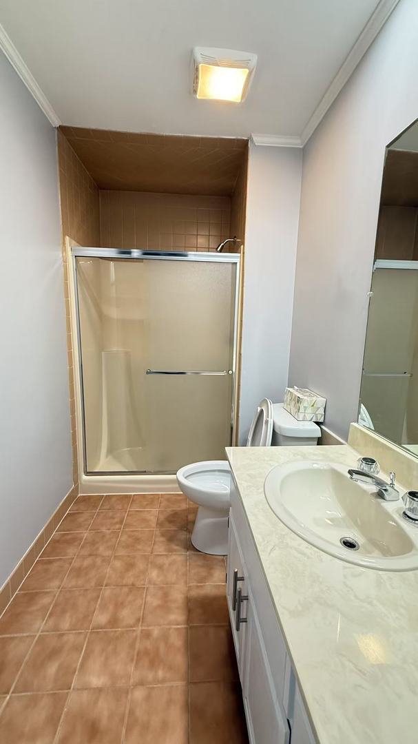 bathroom featuring toilet, a stall shower, tile patterned flooring, and ornamental molding