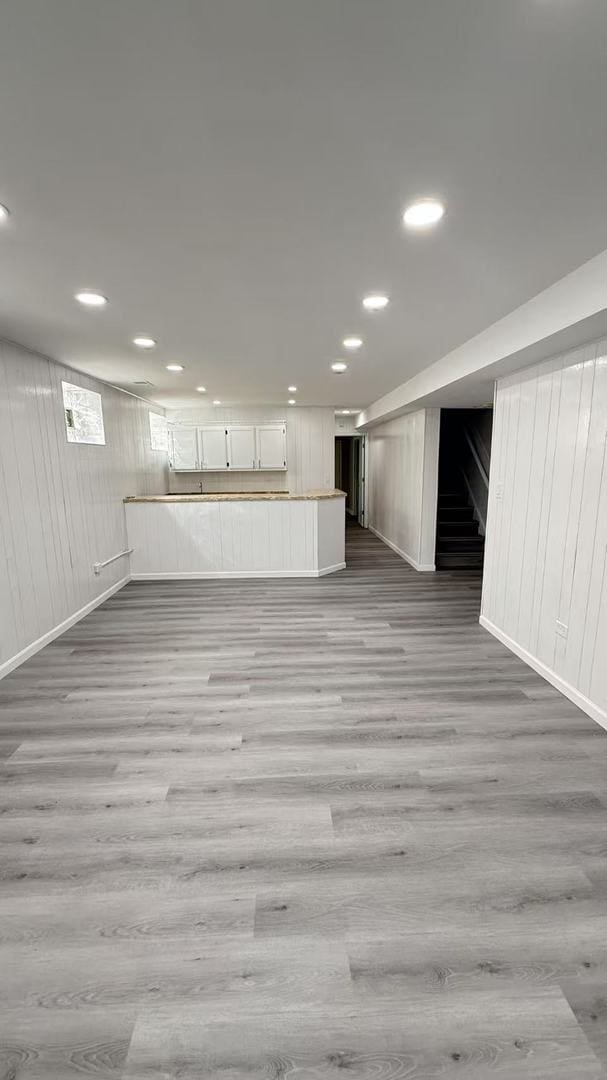 finished basement with recessed lighting, wood walls, baseboards, stairs, and light wood-type flooring