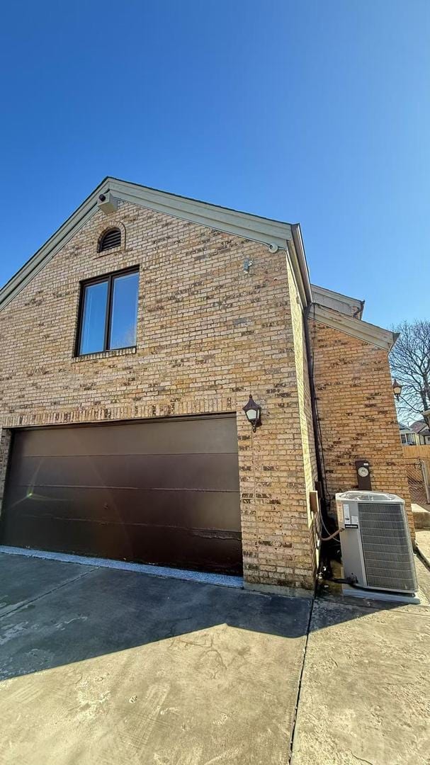 view of side of property with a garage, cooling unit, and brick siding