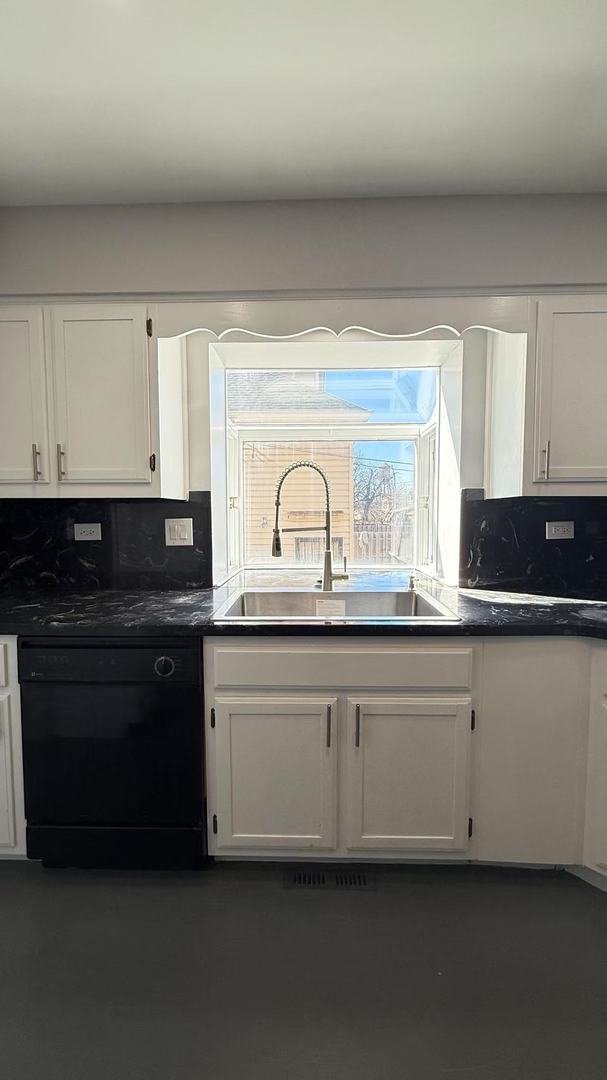 kitchen with dark countertops, black dishwasher, white cabinets, and a sink