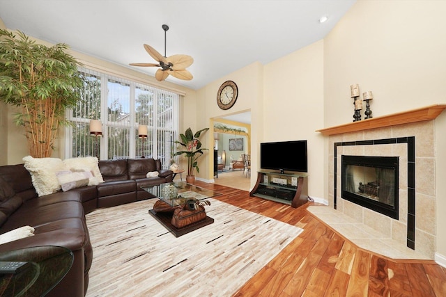 living room featuring wood finished floors, baseboards, a ceiling fan, high vaulted ceiling, and a tiled fireplace