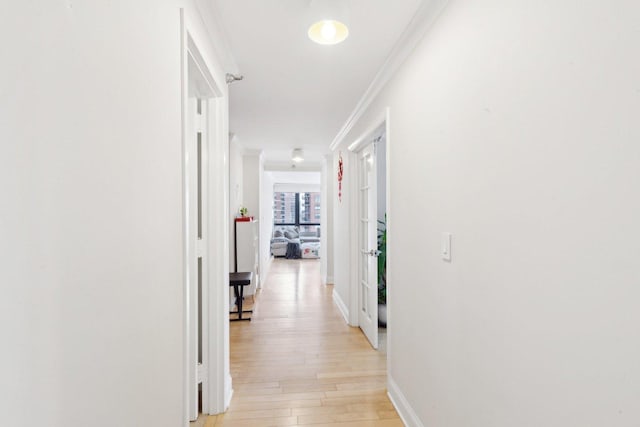 hall with light wood-style flooring, baseboards, and ornamental molding