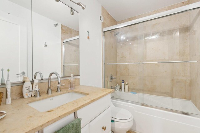 bathroom featuring toilet, vanity, and shower / bath combination with glass door