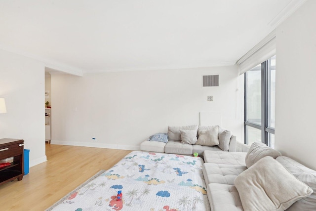 living area with light wood-type flooring, visible vents, baseboards, and ornamental molding