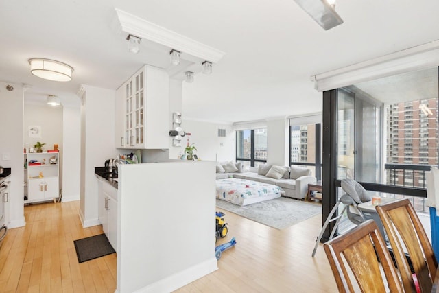 kitchen with light wood-style floors, white cabinets, a wall of windows, glass insert cabinets, and baseboards