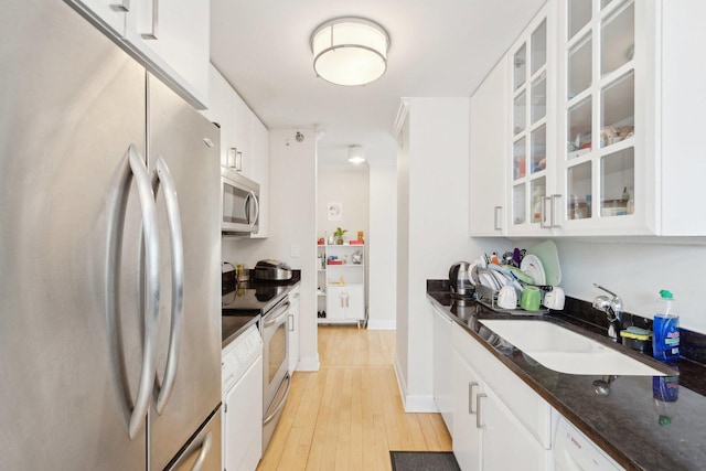 kitchen featuring a sink, stainless steel appliances, white cabinets, glass insert cabinets, and light wood-style floors