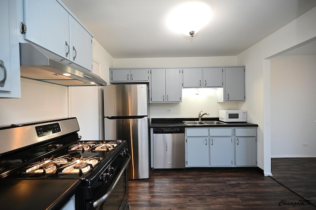 kitchen with under cabinet range hood, stainless steel appliances, a sink, dark countertops, and dark wood finished floors