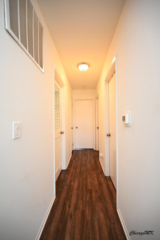 corridor with dark wood-style floors, visible vents, and baseboards