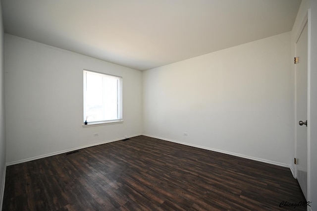 empty room featuring visible vents, dark wood finished floors, and baseboards