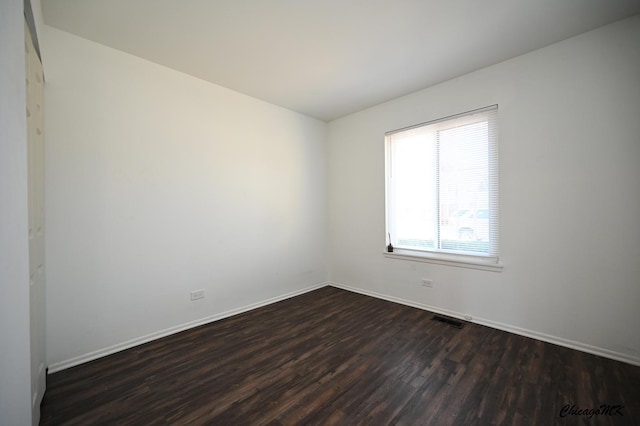 unfurnished room with visible vents, dark wood finished floors, and baseboards