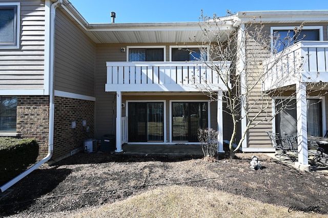 rear view of property featuring a balcony and brick siding