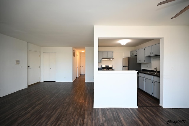 kitchen with under cabinet range hood, a sink, gray cabinets, freestanding refrigerator, and range with gas cooktop