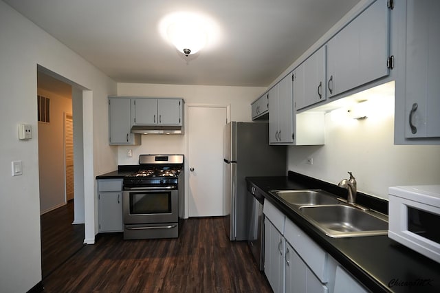 kitchen featuring stainless steel appliances, dark countertops, a sink, and under cabinet range hood