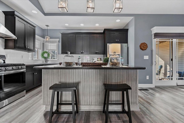 kitchen featuring a kitchen bar, appliances with stainless steel finishes, wall chimney range hood, and light wood finished floors