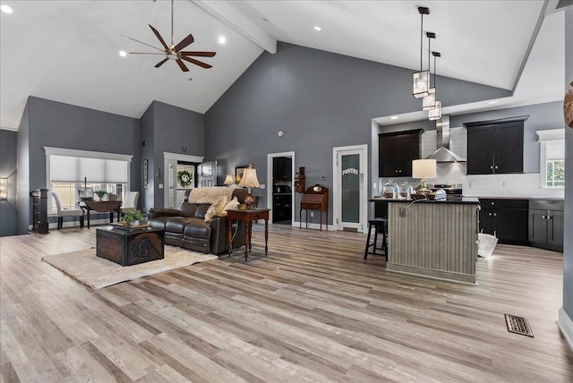 living area with light wood-type flooring, visible vents, beam ceiling, high vaulted ceiling, and a ceiling fan