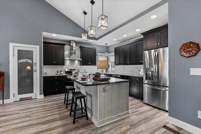 kitchen featuring a breakfast bar, light wood-style flooring, wall chimney exhaust hood, and stainless steel appliances