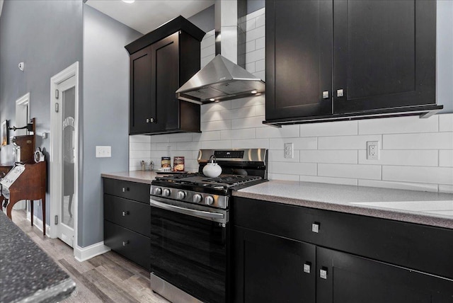 kitchen featuring gas stove, baseboards, light wood-style flooring, wall chimney range hood, and backsplash