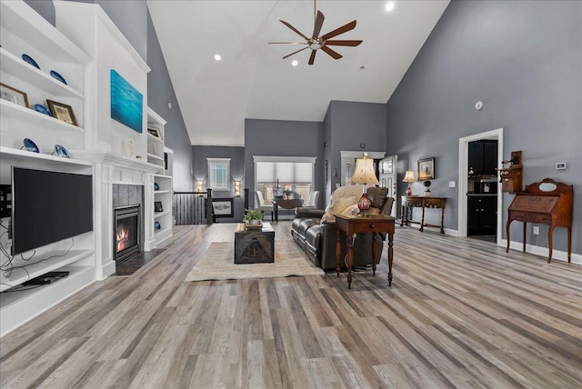 living area featuring a fireplace with flush hearth, built in shelves, a ceiling fan, a high ceiling, and light wood finished floors