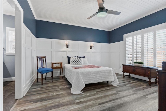 bedroom with wainscoting, wood finished floors, ornamental molding, and a decorative wall