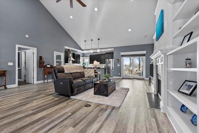 living area featuring high vaulted ceiling, light wood finished floors, a high end fireplace, and ceiling fan