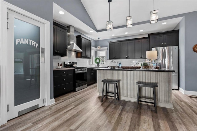 kitchen featuring wall chimney exhaust hood, tasteful backsplash, light wood finished floors, and stainless steel appliances