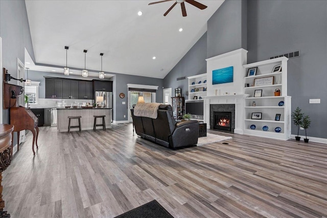 living area with a premium fireplace, high vaulted ceiling, light wood-style flooring, and a ceiling fan