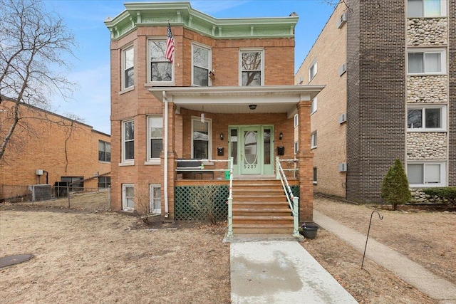 view of front of home featuring a porch, fence, brick siding, and central AC