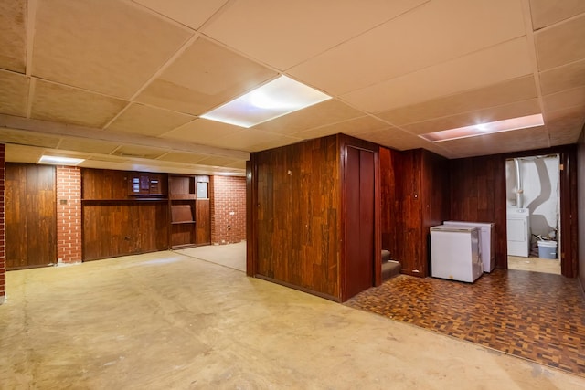 finished below grade area featuring washer / clothes dryer, a drop ceiling, wood walls, and fridge