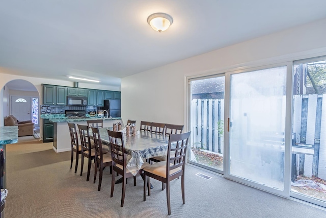 dining area with a healthy amount of sunlight, carpet, visible vents, and arched walkways