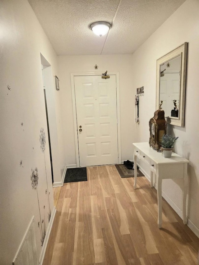 doorway with light wood-type flooring, visible vents, baseboards, and a textured ceiling