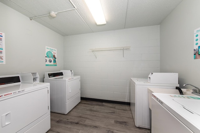 shared laundry area with a textured ceiling, wood finished floors, concrete block wall, and washer and dryer