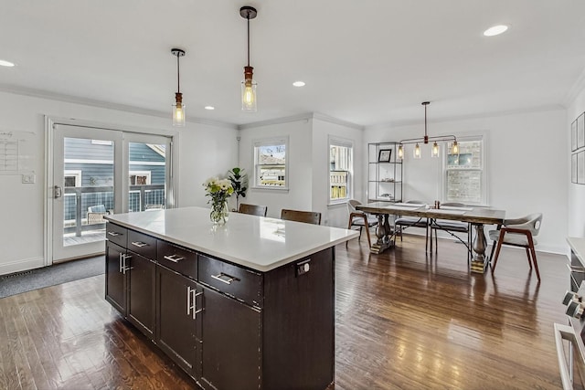 kitchen featuring pendant lighting, dark wood-style floors, crown molding, light countertops, and dark brown cabinets