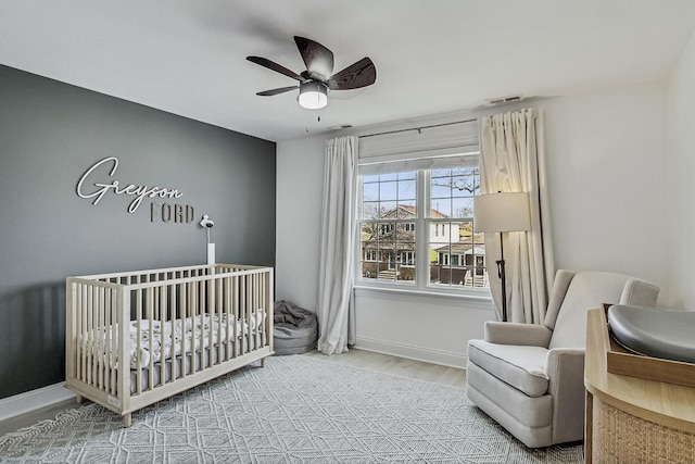 bedroom featuring visible vents, a crib, baseboards, and wood finished floors