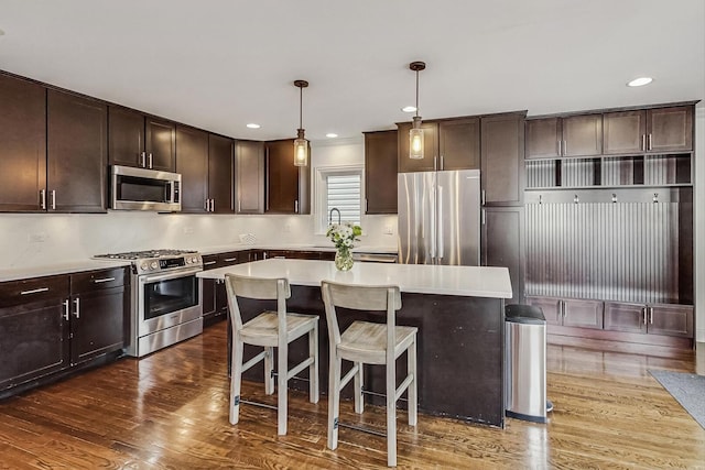 kitchen with dark wood-style floors, stainless steel appliances, dark brown cabinetry, a kitchen bar, and a center island