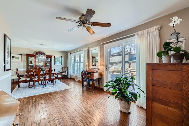 dining room with ceiling fan with notable chandelier, hardwood / wood-style flooring, and baseboards