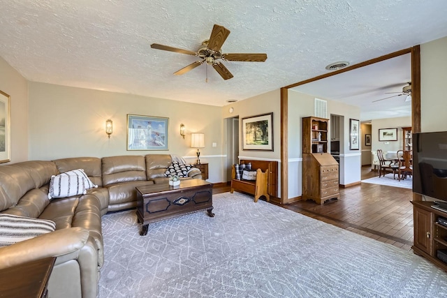 living room with ceiling fan, visible vents, wood-type flooring, and a textured ceiling