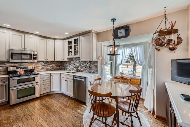 kitchen featuring wood-type flooring, light countertops, backsplash, appliances with stainless steel finishes, and a sink