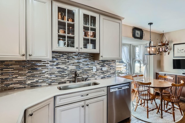 kitchen featuring a sink, light countertops, stainless steel dishwasher, decorative backsplash, and decorative light fixtures