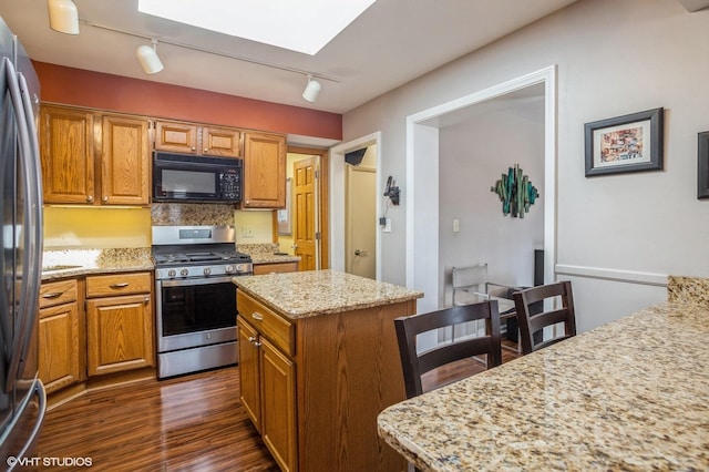 kitchen with light stone countertops, a kitchen island, a skylight, stainless steel appliances, and dark wood-type flooring