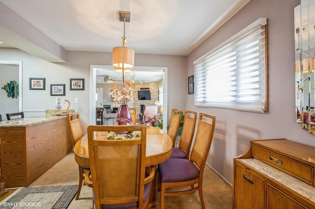 dining area with ceiling fan, light colored carpet, and a large fireplace