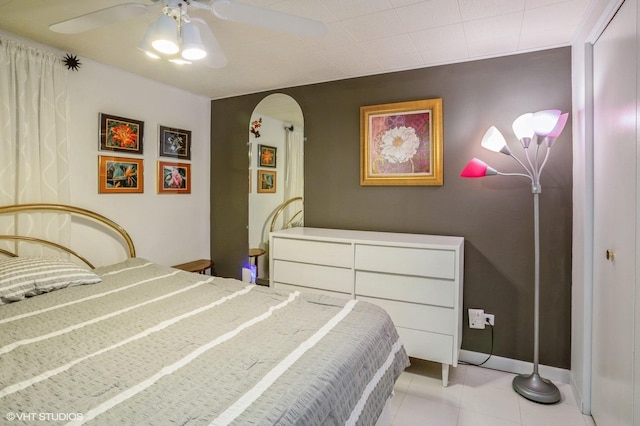 bedroom featuring light tile patterned flooring, a ceiling fan, arched walkways, and baseboards