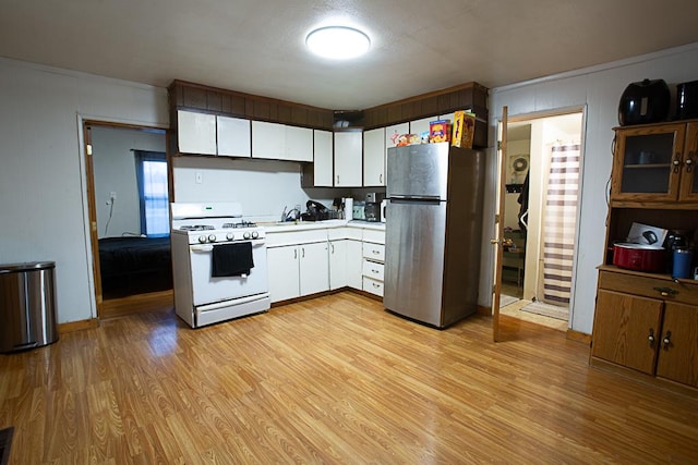 kitchen with light wood finished floors, white range with gas cooktop, freestanding refrigerator, light countertops, and white cabinetry