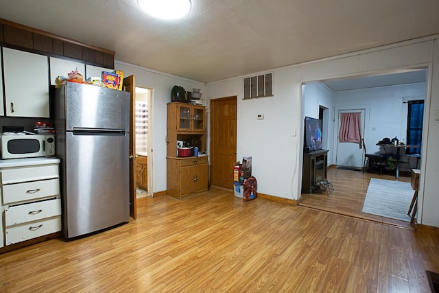 kitchen featuring visible vents, white microwave, light wood-style floors, freestanding refrigerator, and baseboards